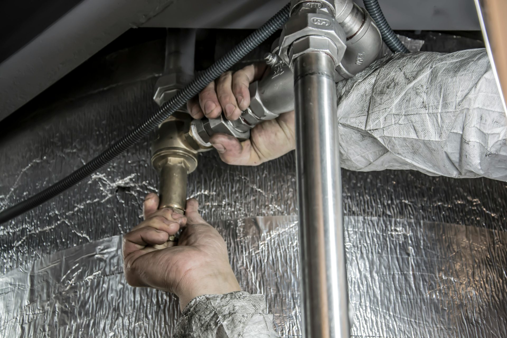 Nahaufnahme der Hände eines Klempners bei der Installation von Stahlrohren in Innenräumen, die geschickte Handwerkskunst demonstriert.